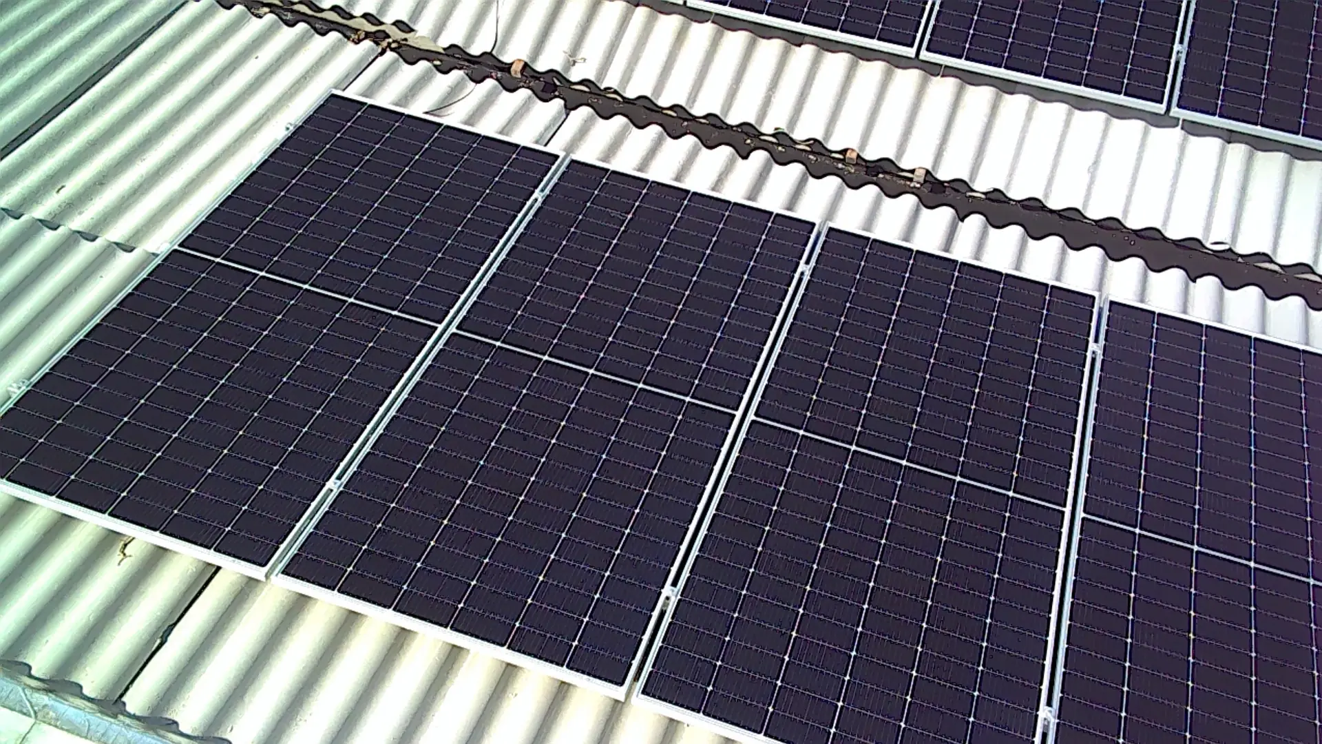 Close de fileiras de módulos fotovoltaicos instalados sobre telhado metálico